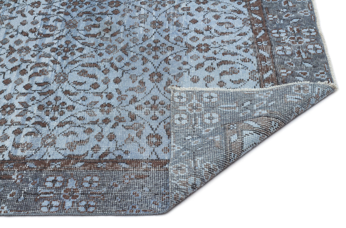 Light blue and brown traditional floral medallion rug with a folded corner showing the woven backing.