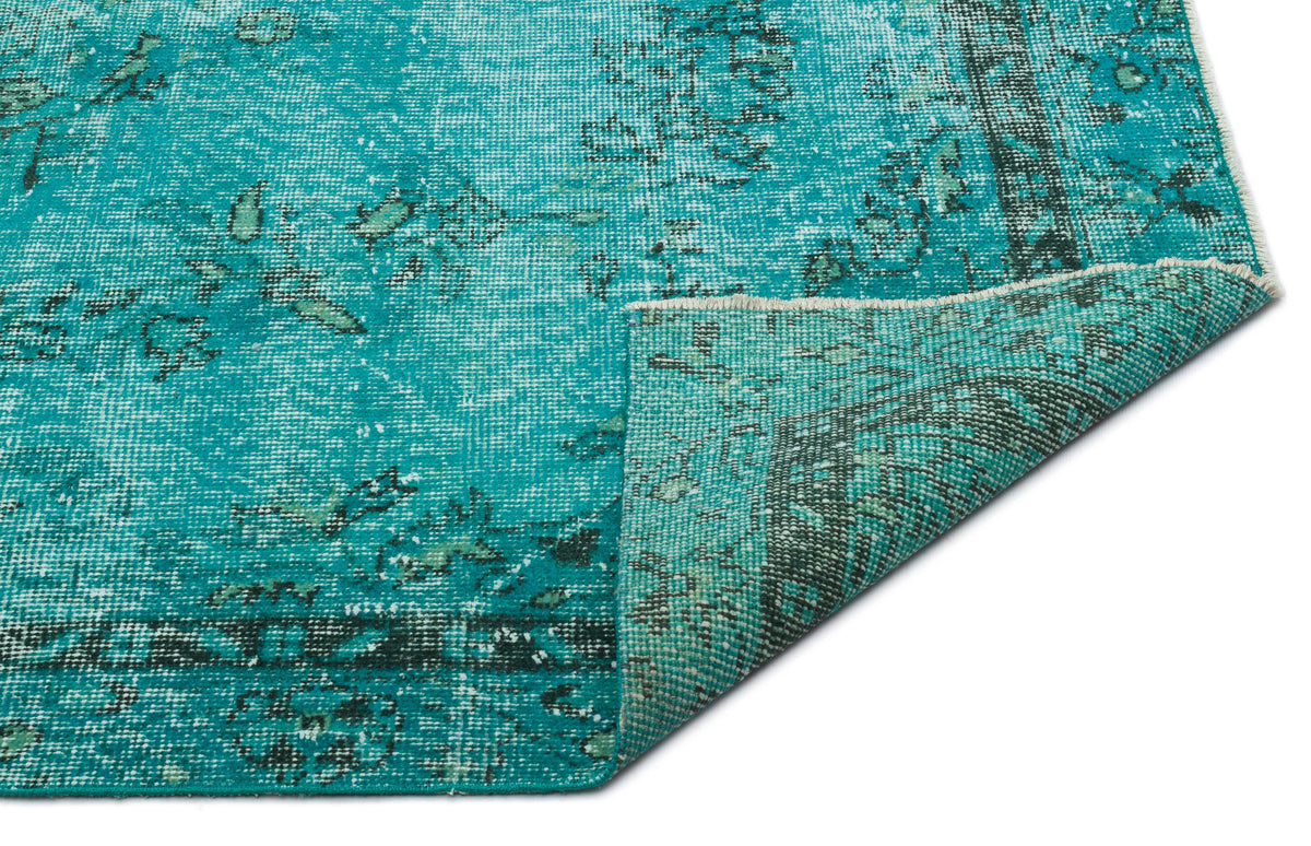 Teal and dark green distressed vintage-style rug with a folded corner showing the woven backing.