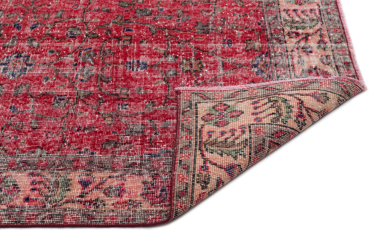 Red and beige vintage-style rug with a distressed floral medallion pattern and a folded corner on a white background.