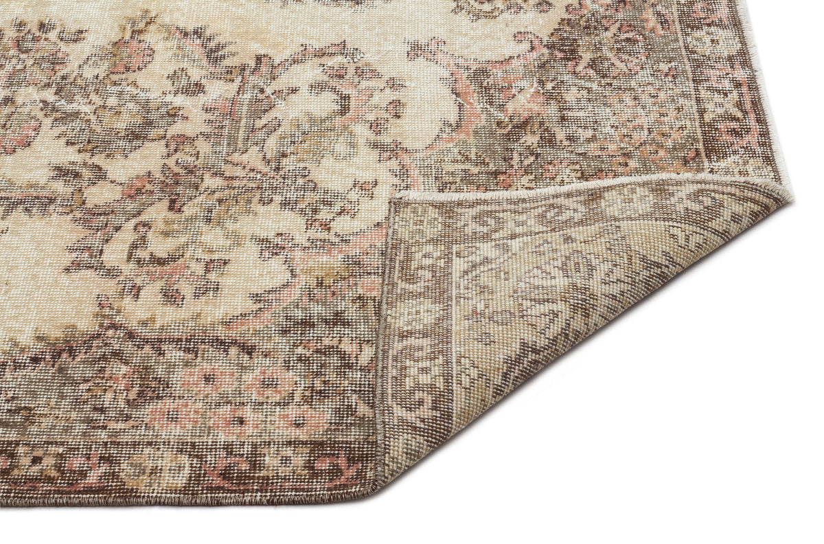 Beige, brown, and muted pink vintage-style rug with a floral medallion pattern, shown with a corner folded over.