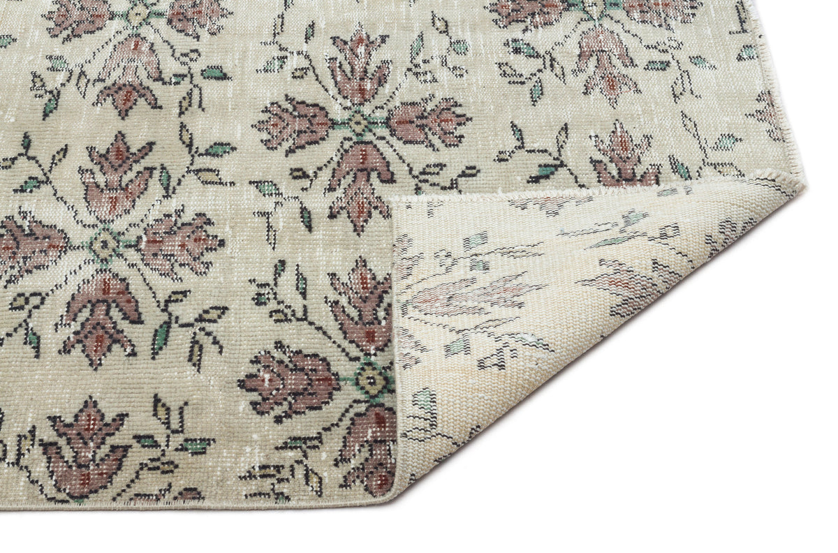 Beige rug with a faded floral medallion pattern in muted red and green, shown with a corner folded over.