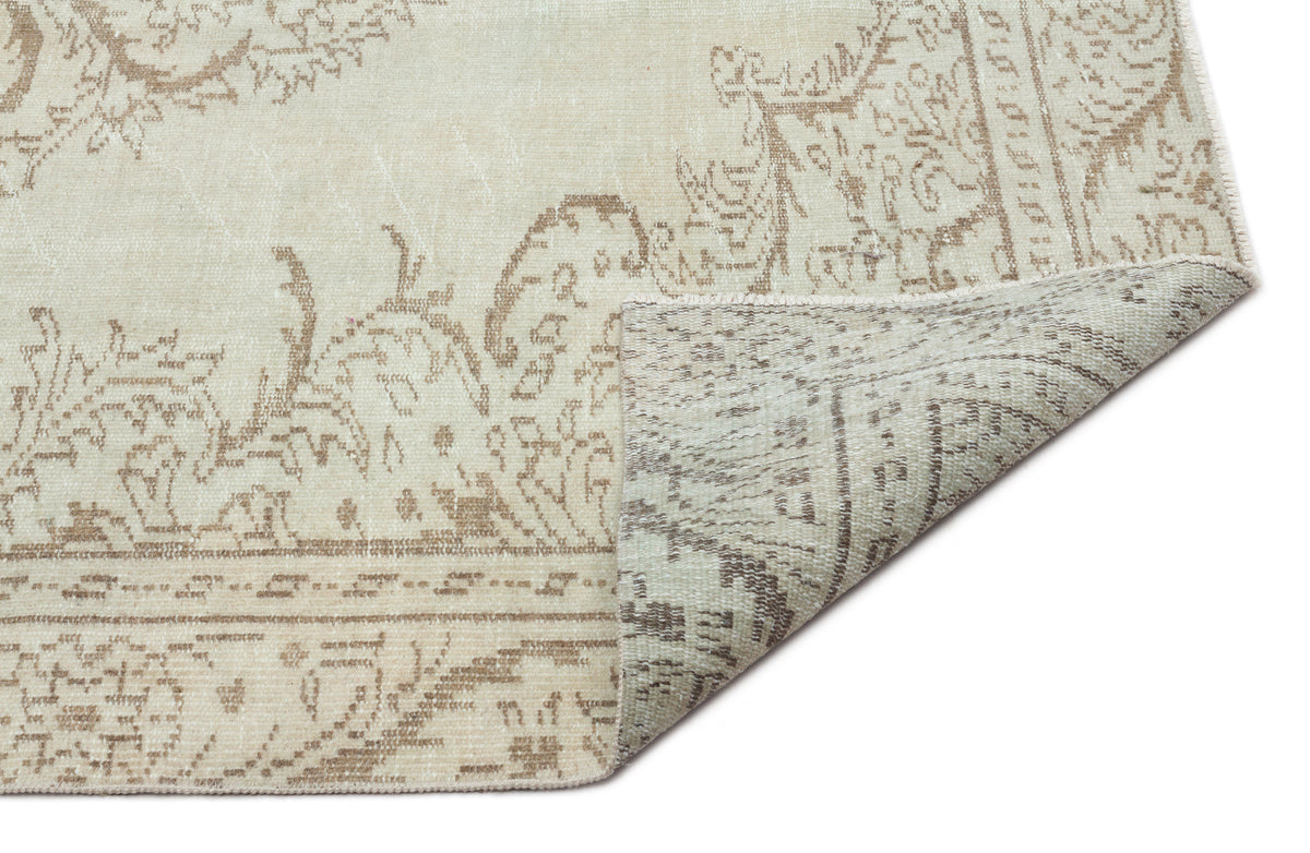 Beige and taupe vintage-style rug with a faded floral medallion pattern, shown with a corner folded over.