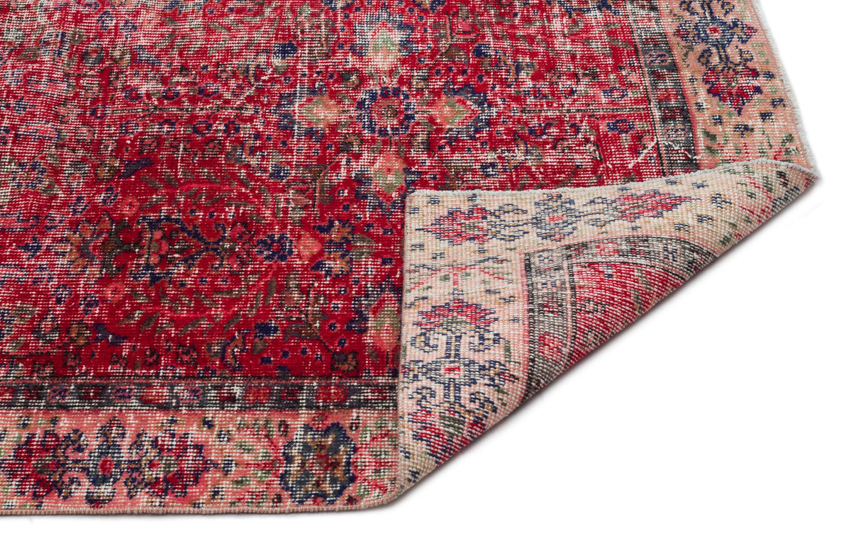 Distressed red Persian-style rug with blue and cream floral patterns and a folded corner on a white background.