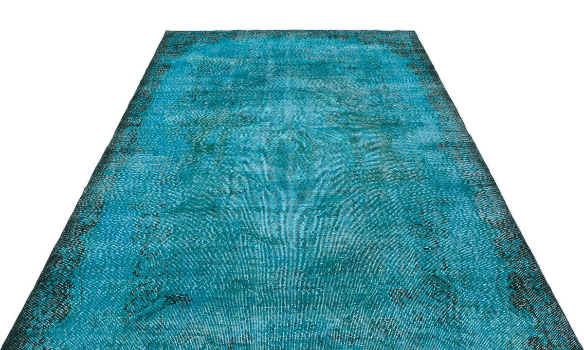 Distressed turquoise and black overdyed rug with a faded traditional medallion pattern on a white background.