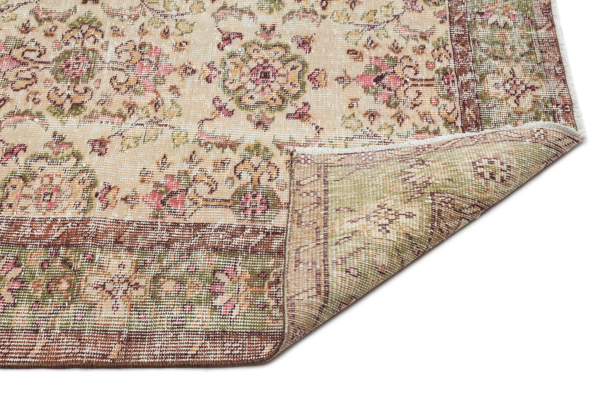 Beige rug with a distressed floral medallion pattern in pink, green, and brown, featuring a folded corner.