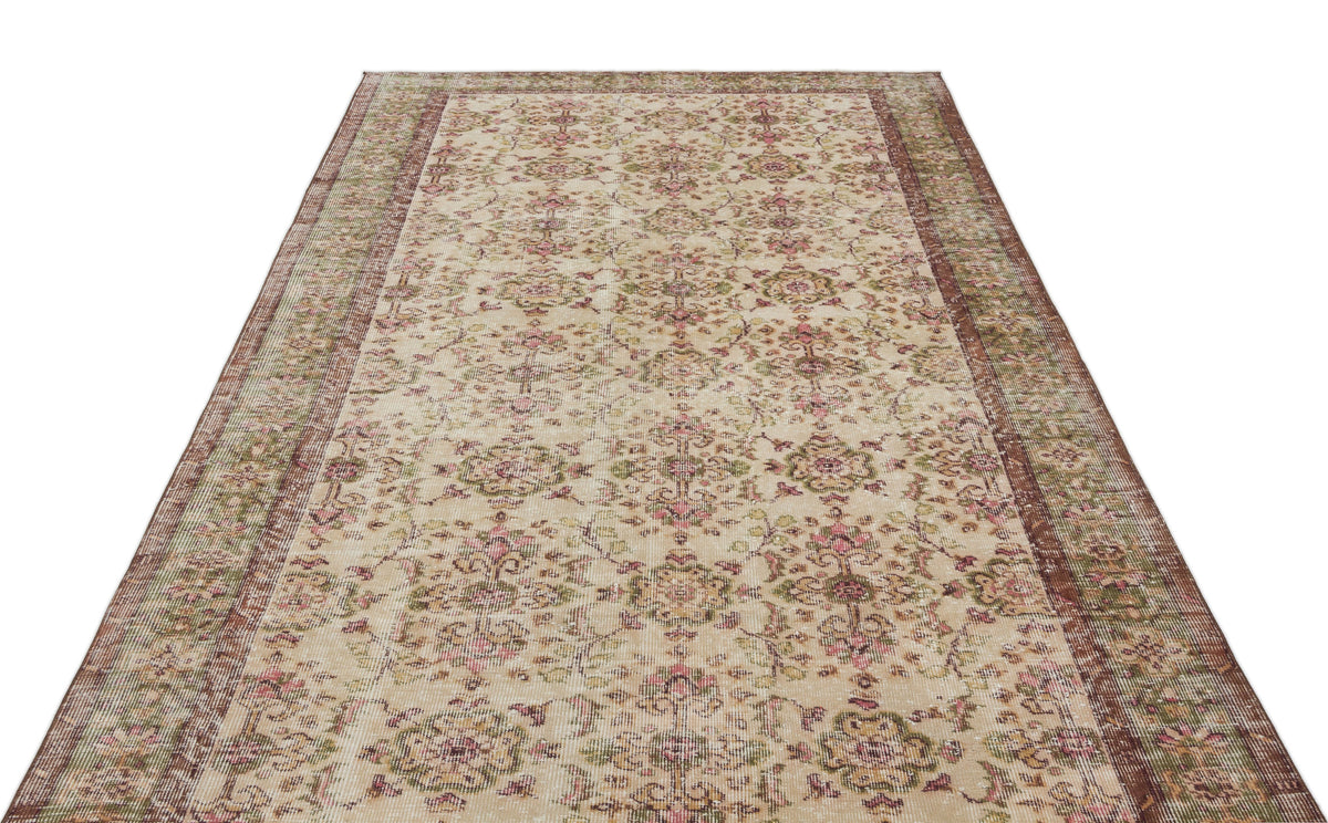 Beige vintage-style rug with a distressed floral medallion pattern in muted pink and green, isolated on white.