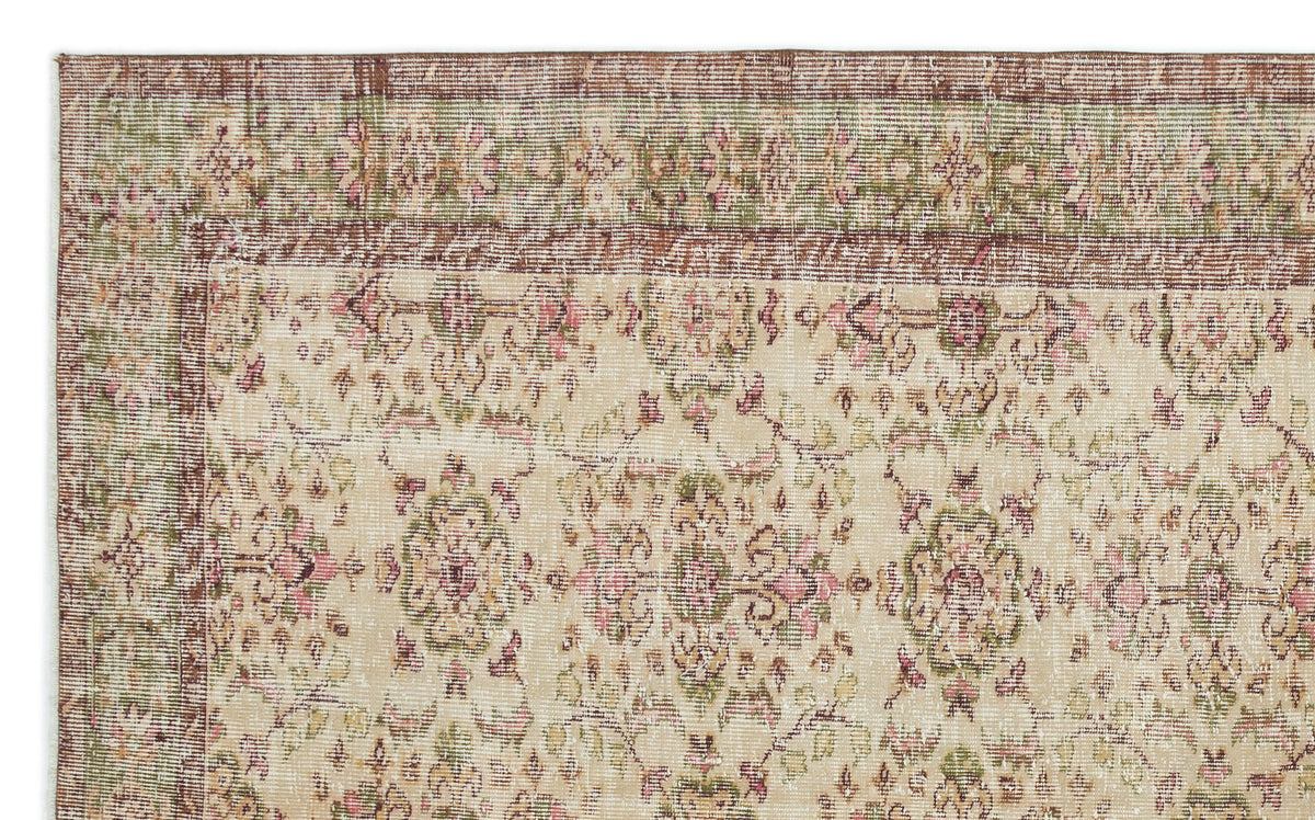 Distressed beige rug with a faded floral medallion pattern in muted pink, green, and brown tones.