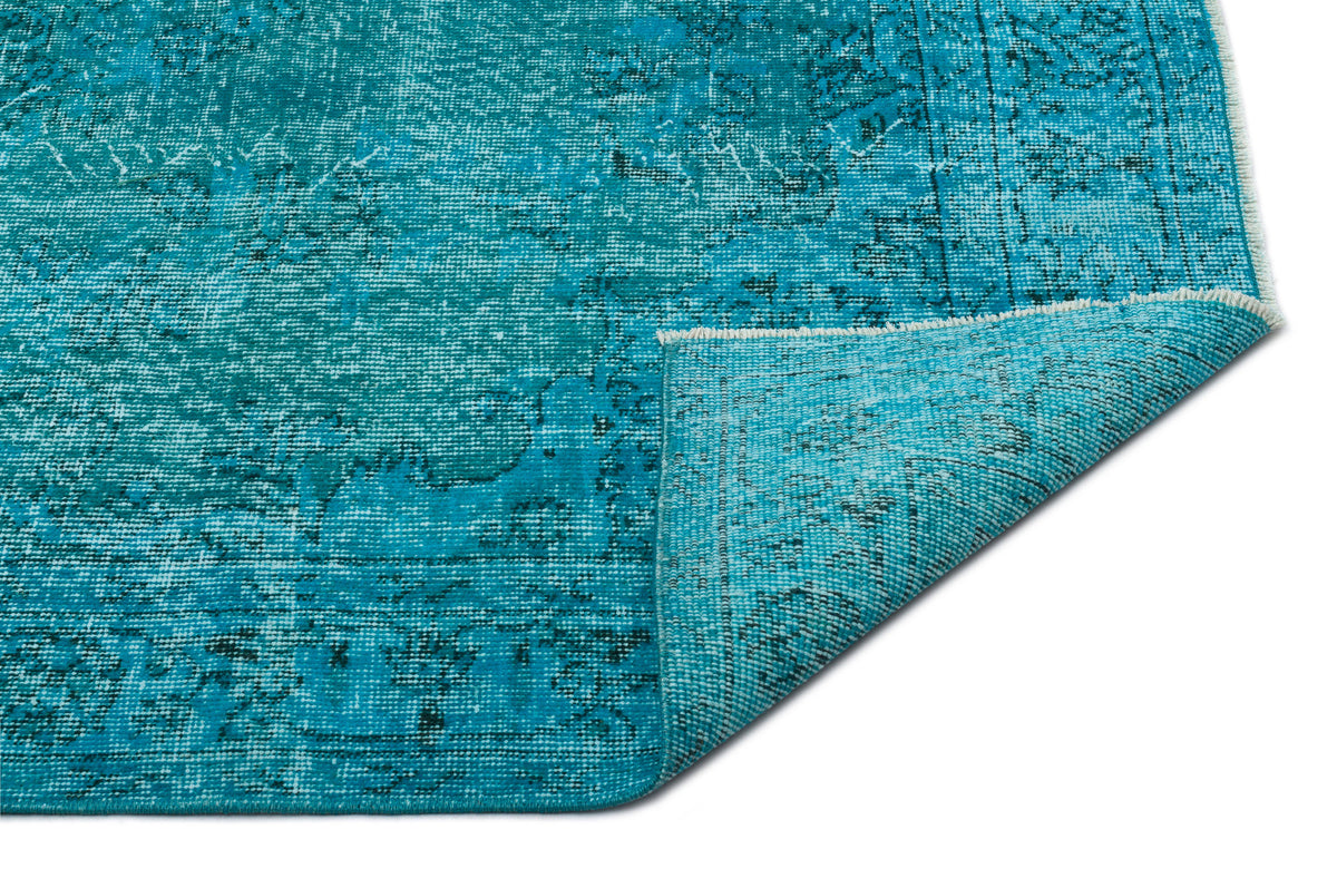 Turquoise distressed rug with a faded traditional pattern and a folded corner, isolated on a white background.