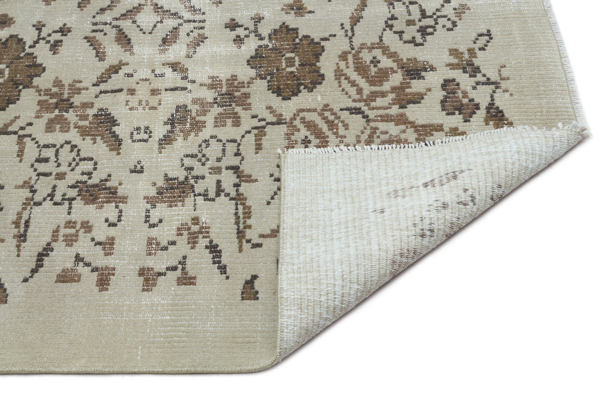 Beige and brown floral patterned rug with a distressed finish and a folded corner showing the underside texture.