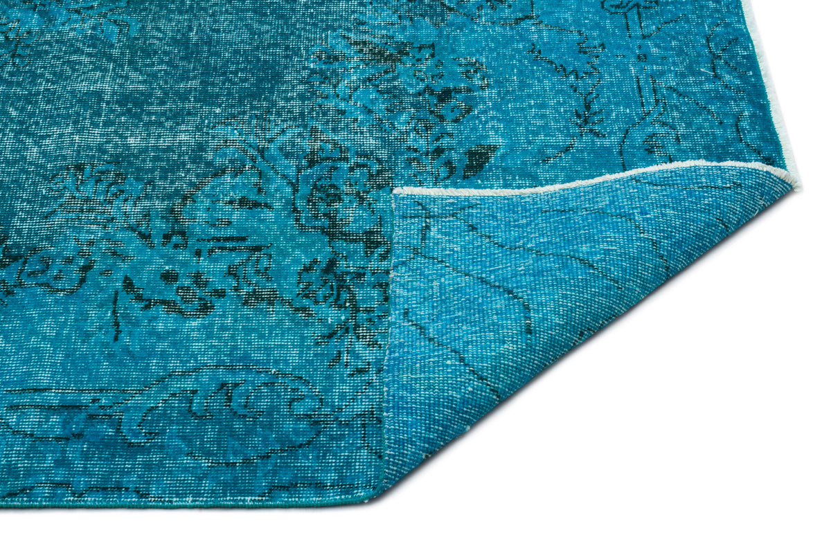 Bright turquoise rug with a distressed black floral pattern and a folded corner showing the woven backing.