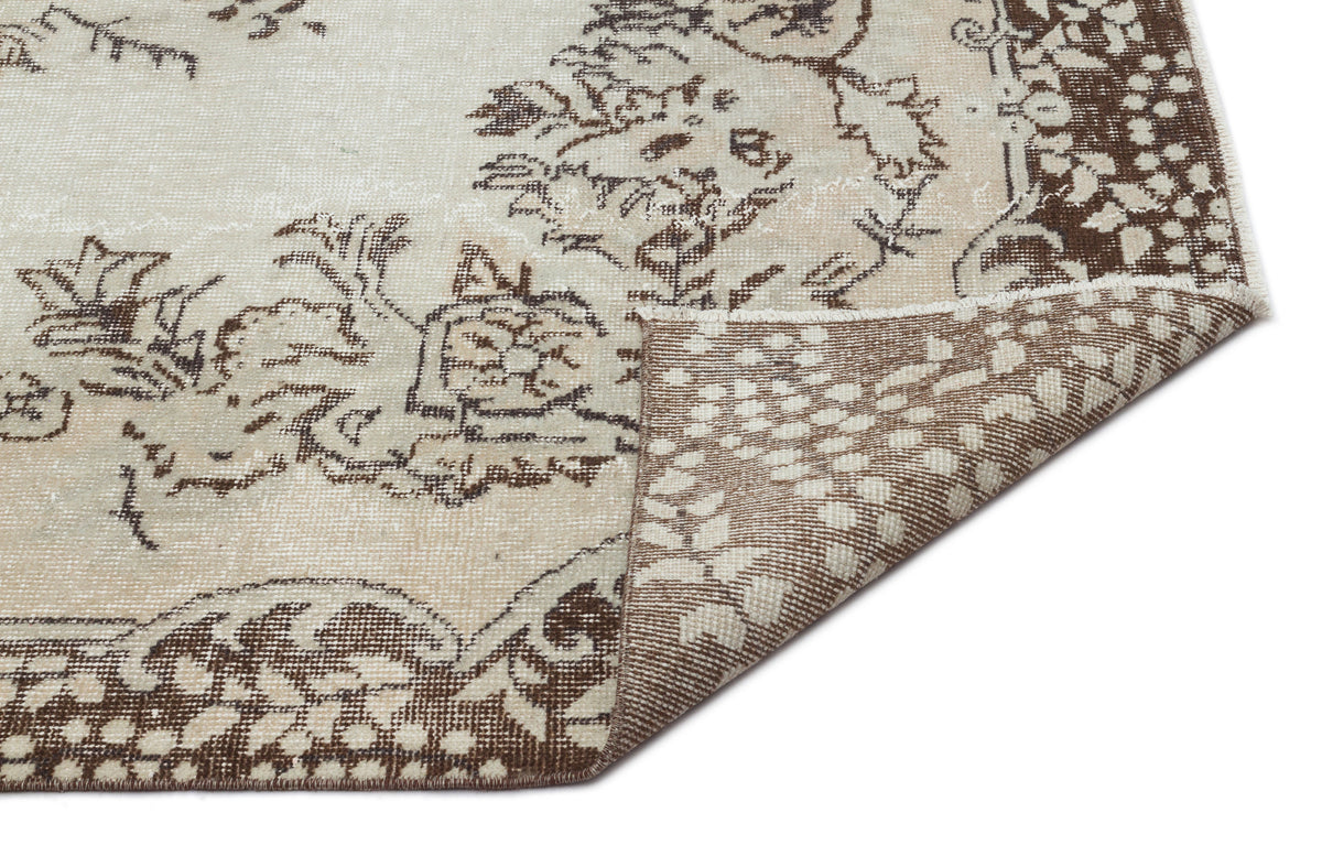 Beige and brown distressed rug with a floral medallion pattern, shown with a corner folded over on a white background.