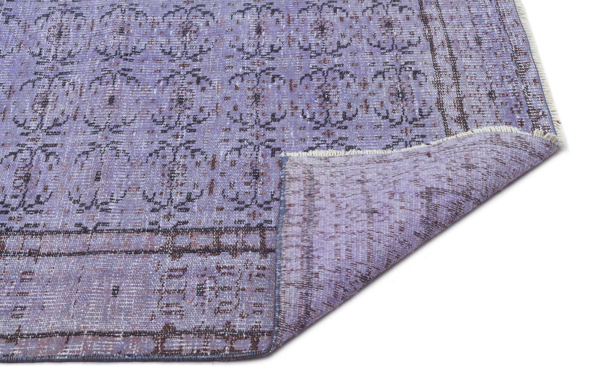 Lavender and charcoal distressed rug with a repeating floral medallion pattern and a folded corner showing the backing.