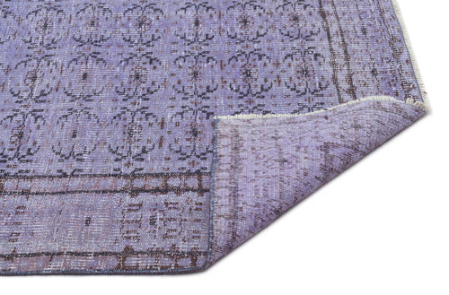 Load image 1 in gallery view. Lavender and charcoal distressed rug with a repeating floral medallion pattern and a folded corner showing the backing.