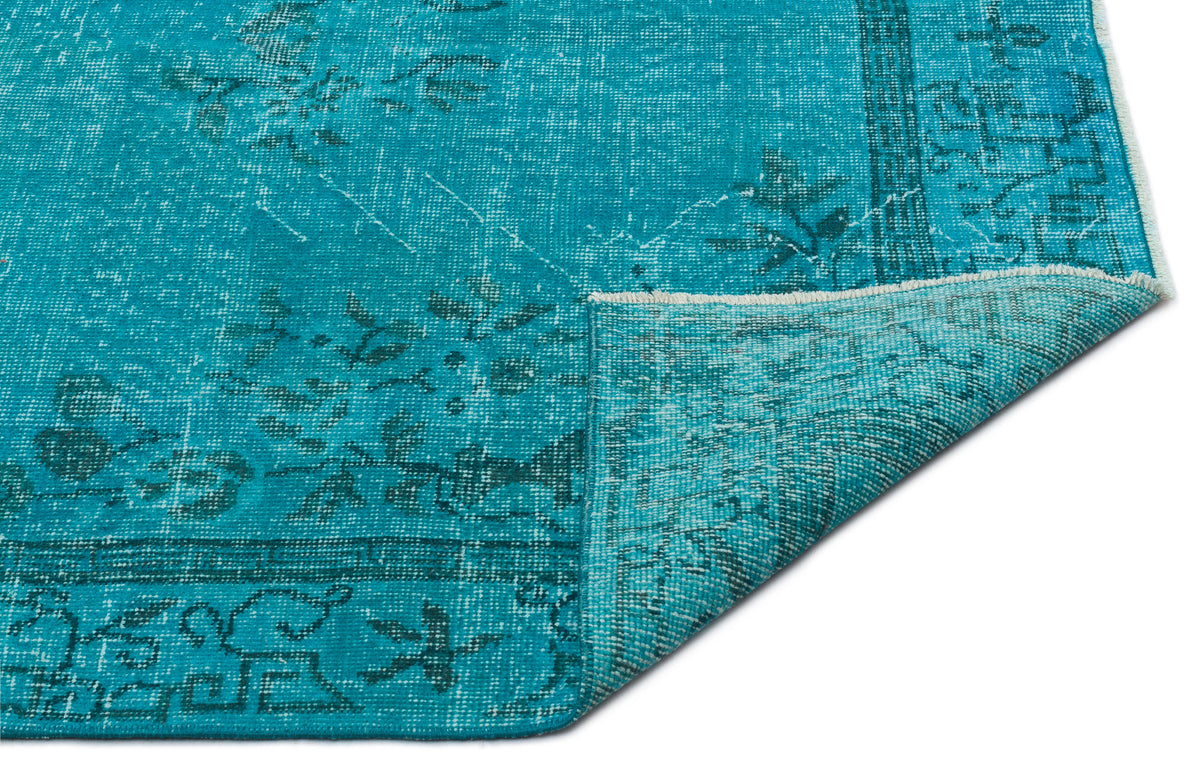 Turquoise distressed rug with a faded floral medallion pattern and a folded corner, isolated on a white background.