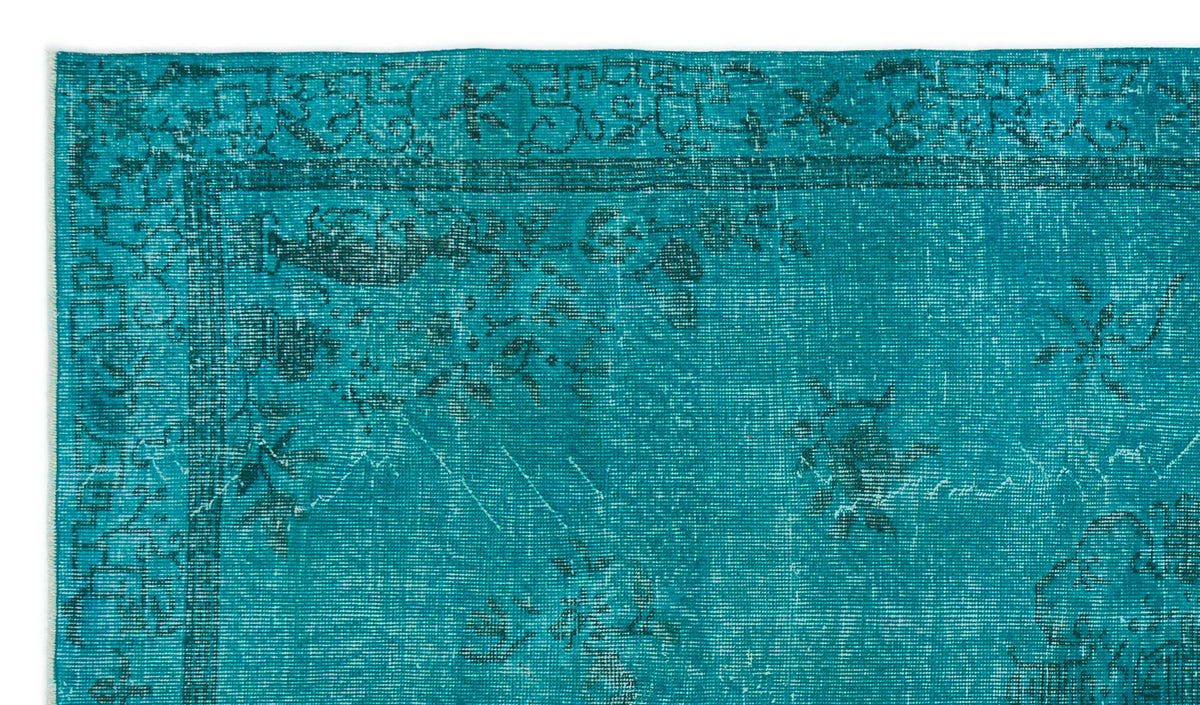 Teal rug with a distressed, dark floral border and scattered botanical motifs on a white background.