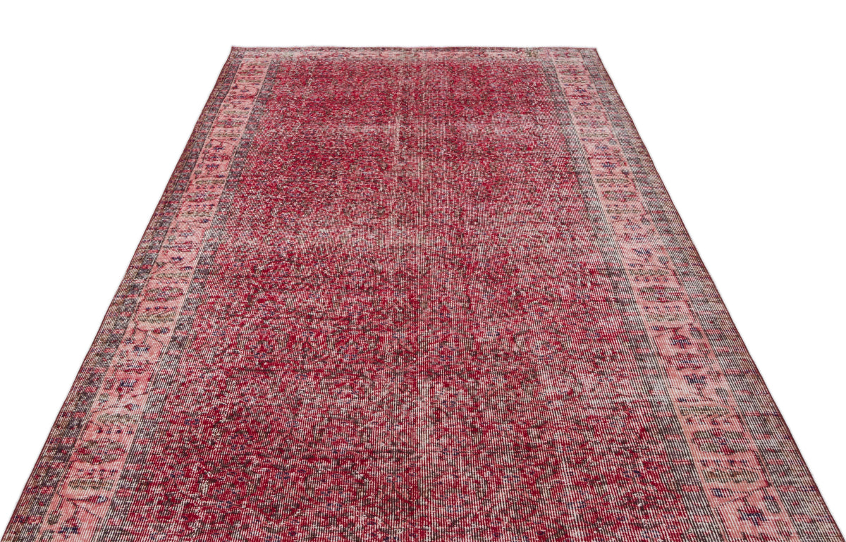 Distressed crimson and pink vintage-style rug with a faded central field and ornate geometric border.