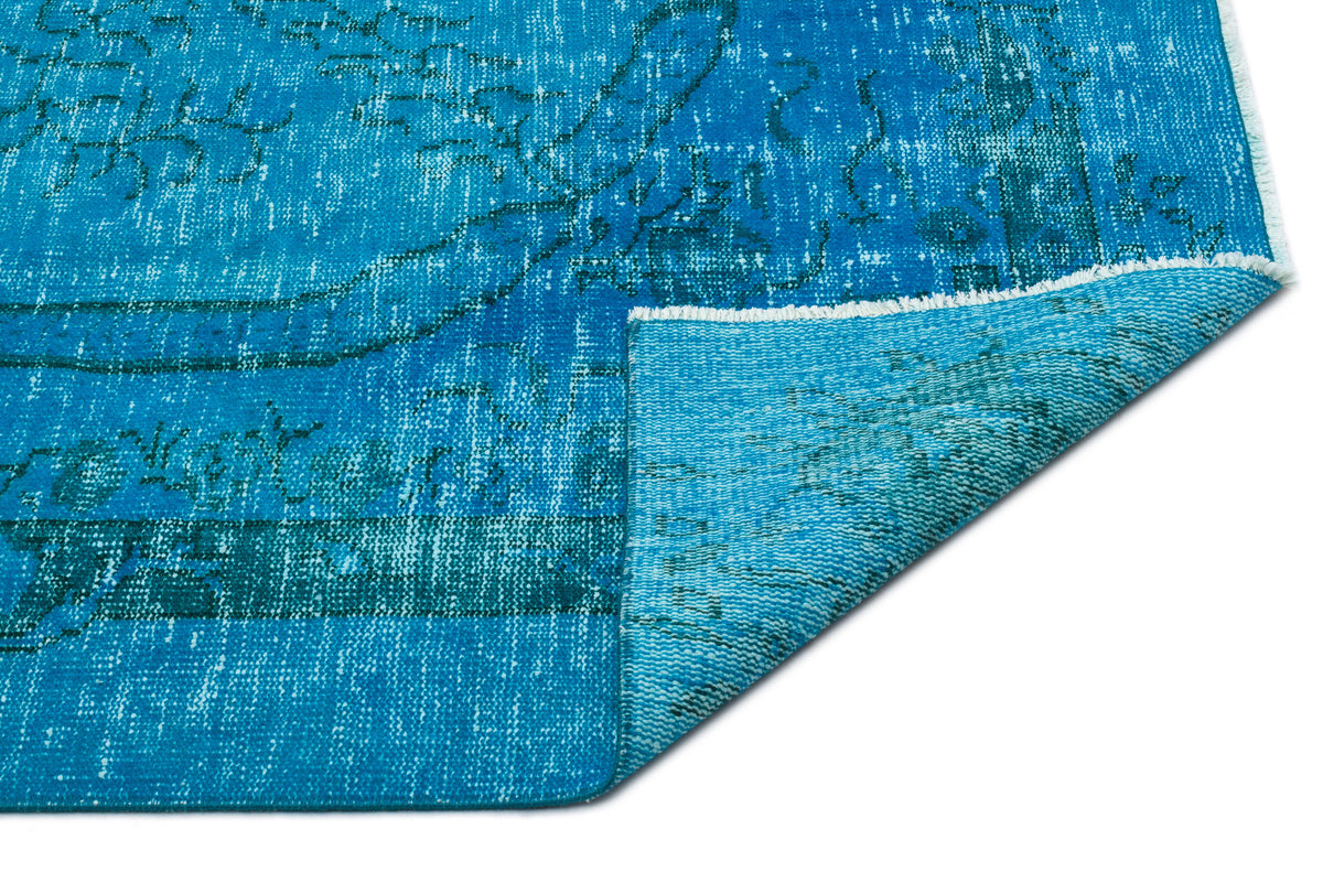 Bright blue distressed rug with a faded traditional pattern and a folded corner showing the underside.