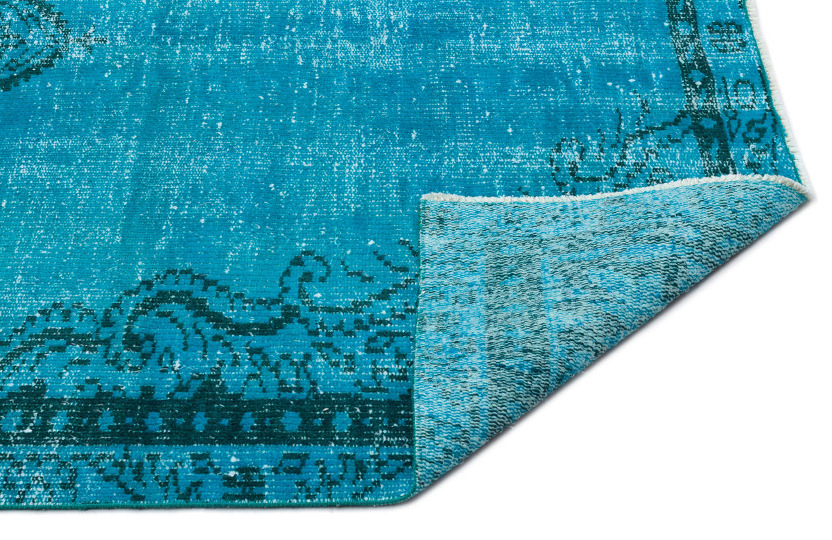 Bright turquoise distressed rug with a dark teal traditional border pattern, shown with a folded corner on white.