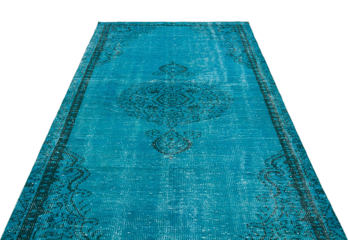 Bright turquoise distressed rug with a dark charcoal central medallion and ornate border pattern on a white background.