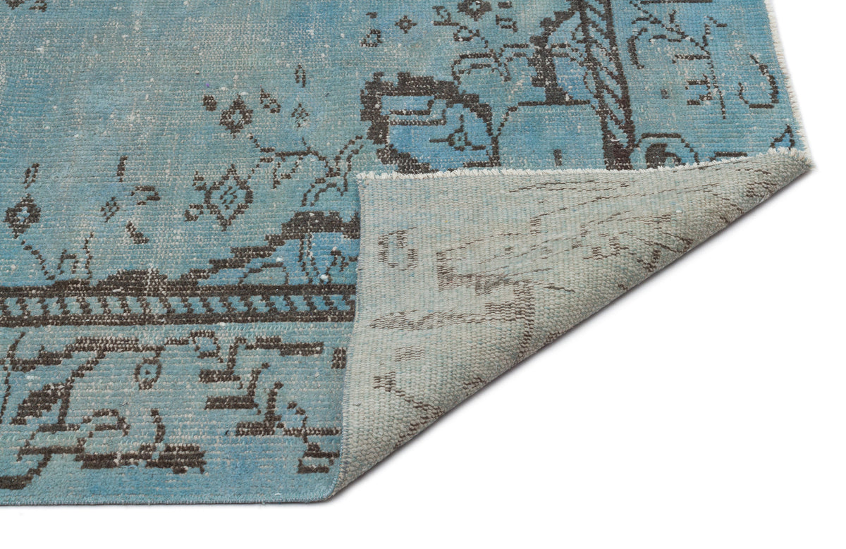 Distressed light blue rug with a dark grey traditional floral pattern, shown with a corner folded over on white.