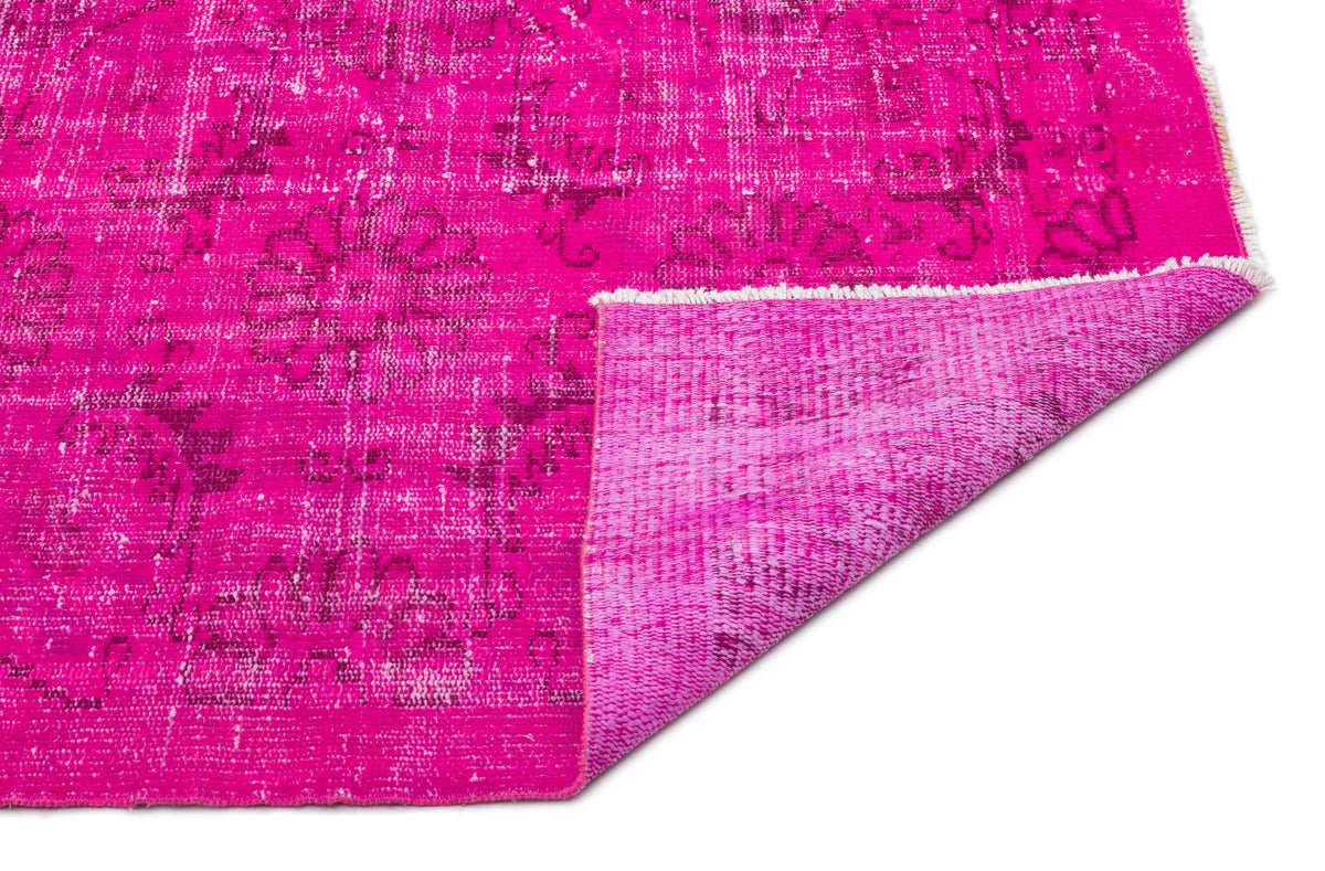 Hot pink distressed rug with a faded floral medallion pattern and a folded corner showing the textured underside.