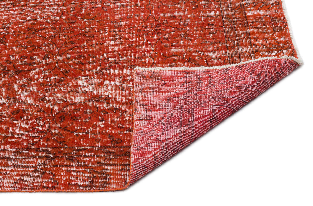 Distressed rust-red rug with a faded traditional pattern and a folded corner showing the woven backing.