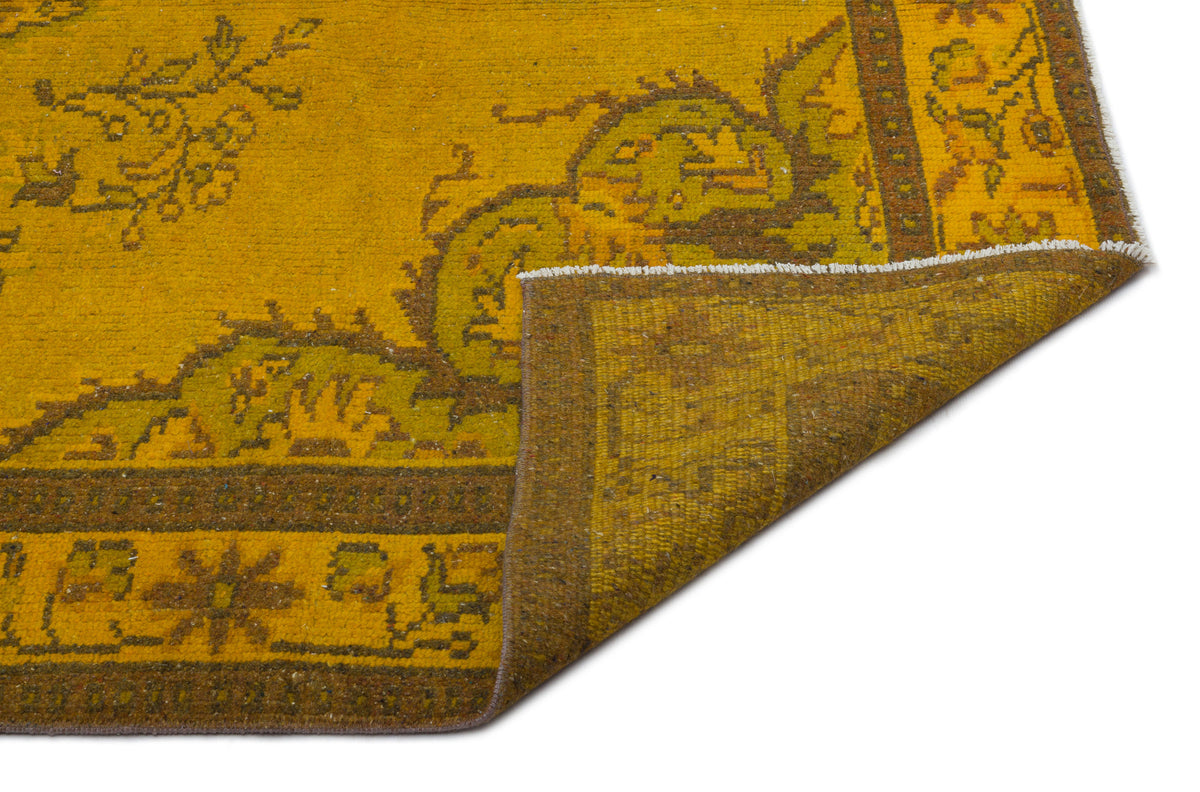 Mustard yellow and olive green traditional rug with a floral border, shown with a corner folded over.