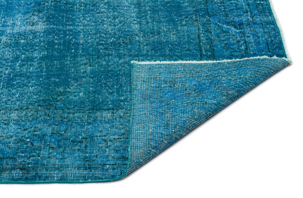Distressed teal blue rug with a faded geometric pattern and a folded corner, isolated on a white background.
