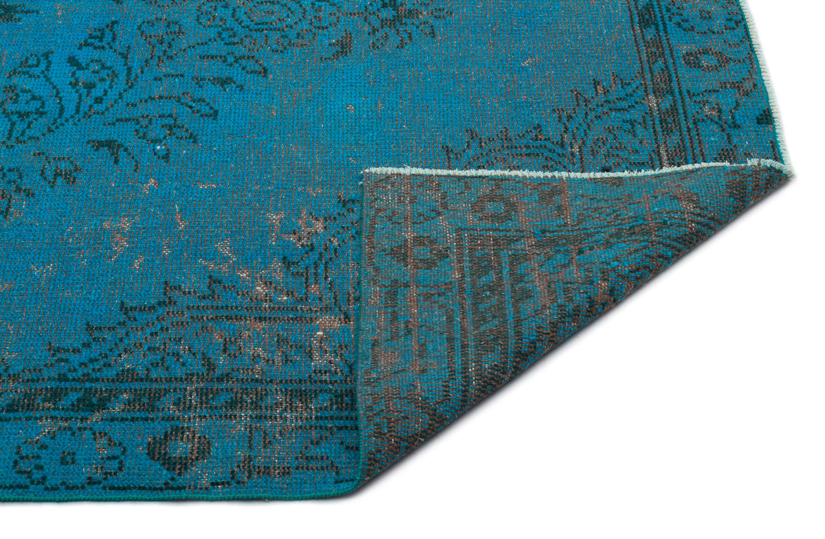 Turquoise and charcoal distressed rug with a traditional floral medallion pattern, shown with a folded corner.