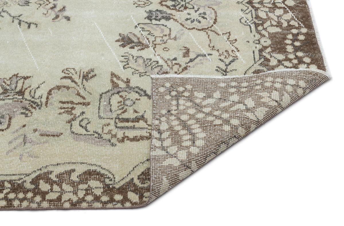 Beige and brown distressed rug with a faded floral medallion pattern, shown with a corner folded over.