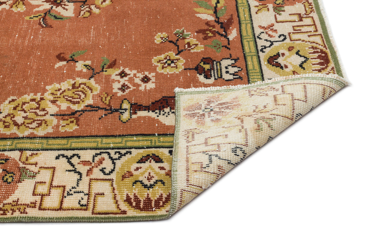 Terracotta rug with floral motifs and a cream border, featuring a folded corner revealing the woven underside.