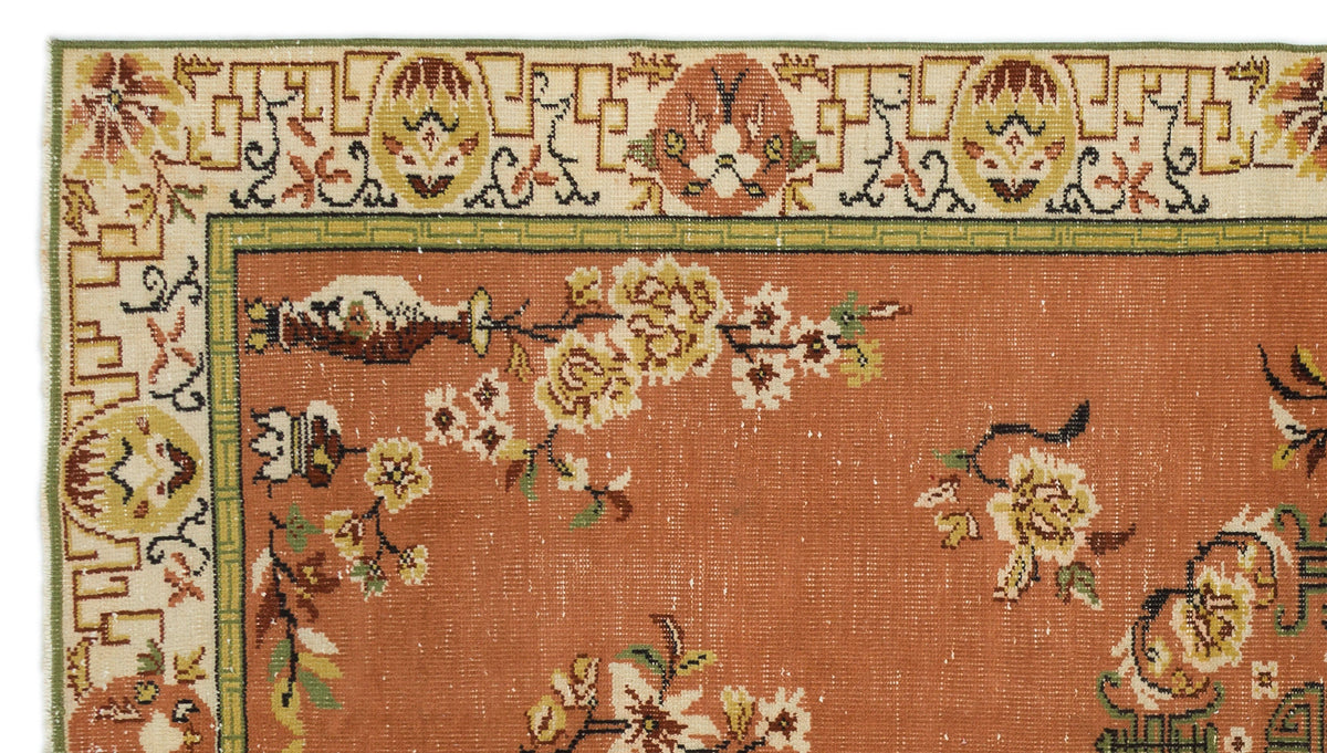 Terracotta rug with floral branch motifs and a cream geometric border, isolated on a white background.