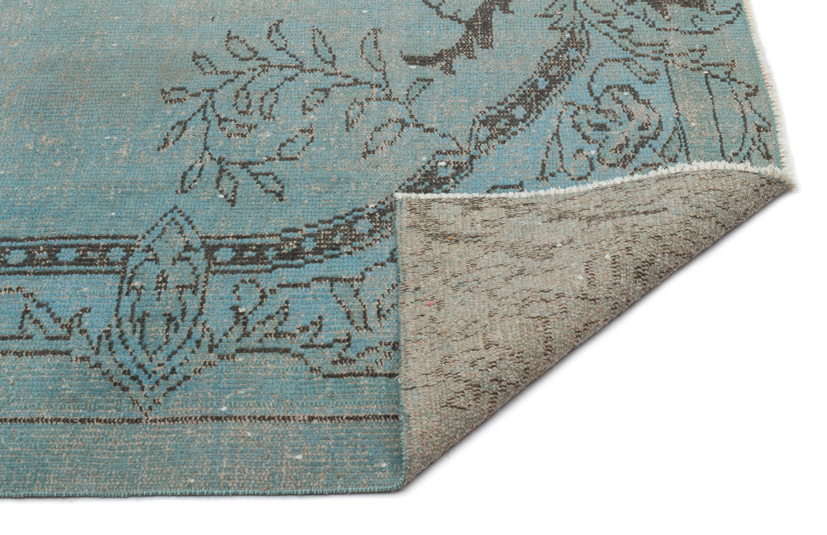 Blue and charcoal distressed traditional rug with a floral medallion pattern, shown with a corner folded over.