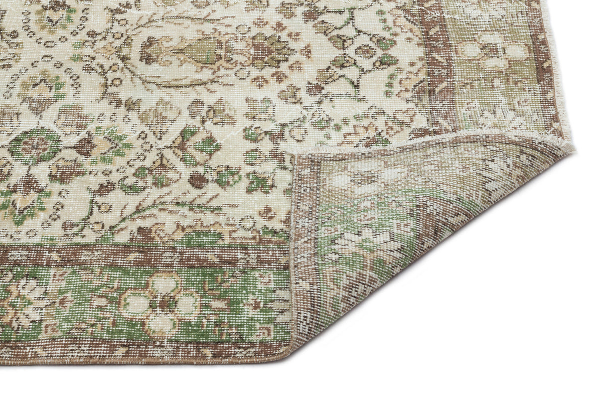 Cream, green, and brown vintage-style rug with a floral medallion pattern and a folded corner showing the underside.