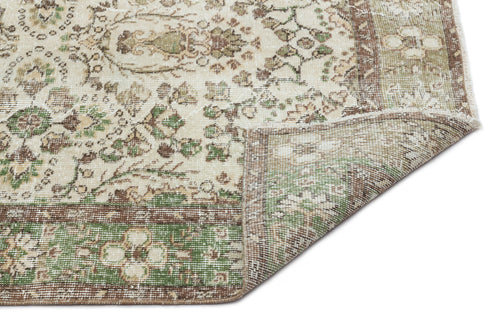 Load image 1 in gallery view. Cream, green, and brown vintage-style rug with a floral medallion pattern and a folded corner showing the underside.