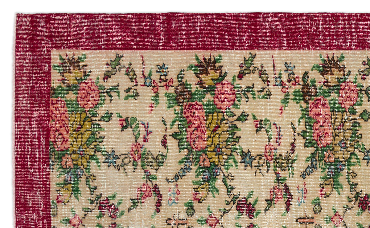 Distressed beige rug with a deep red border and a repeating floral pattern in pink, green, and yellow.