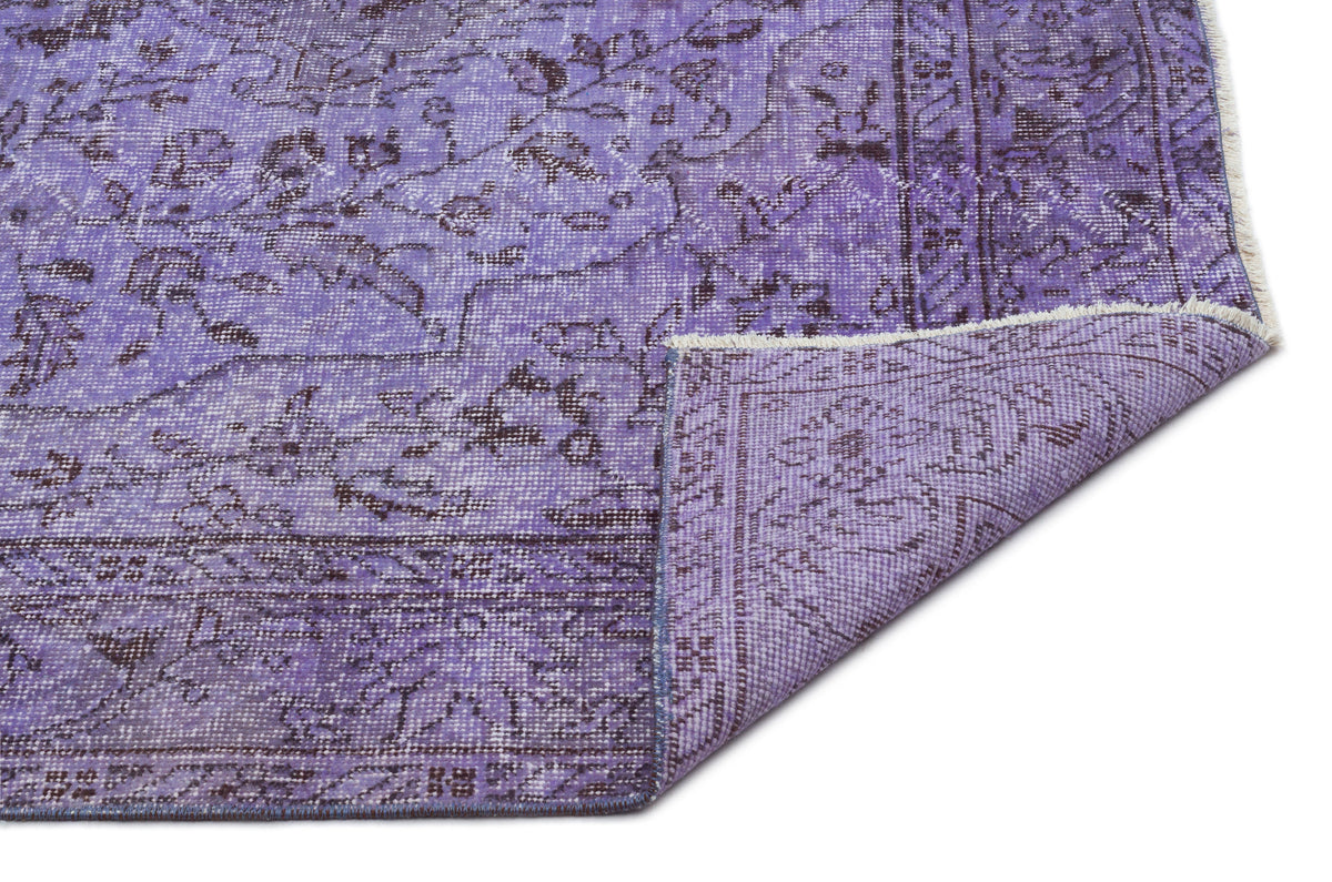 Distressed purple rug with a dark floral medallion pattern and a folded corner showing the woven backing.