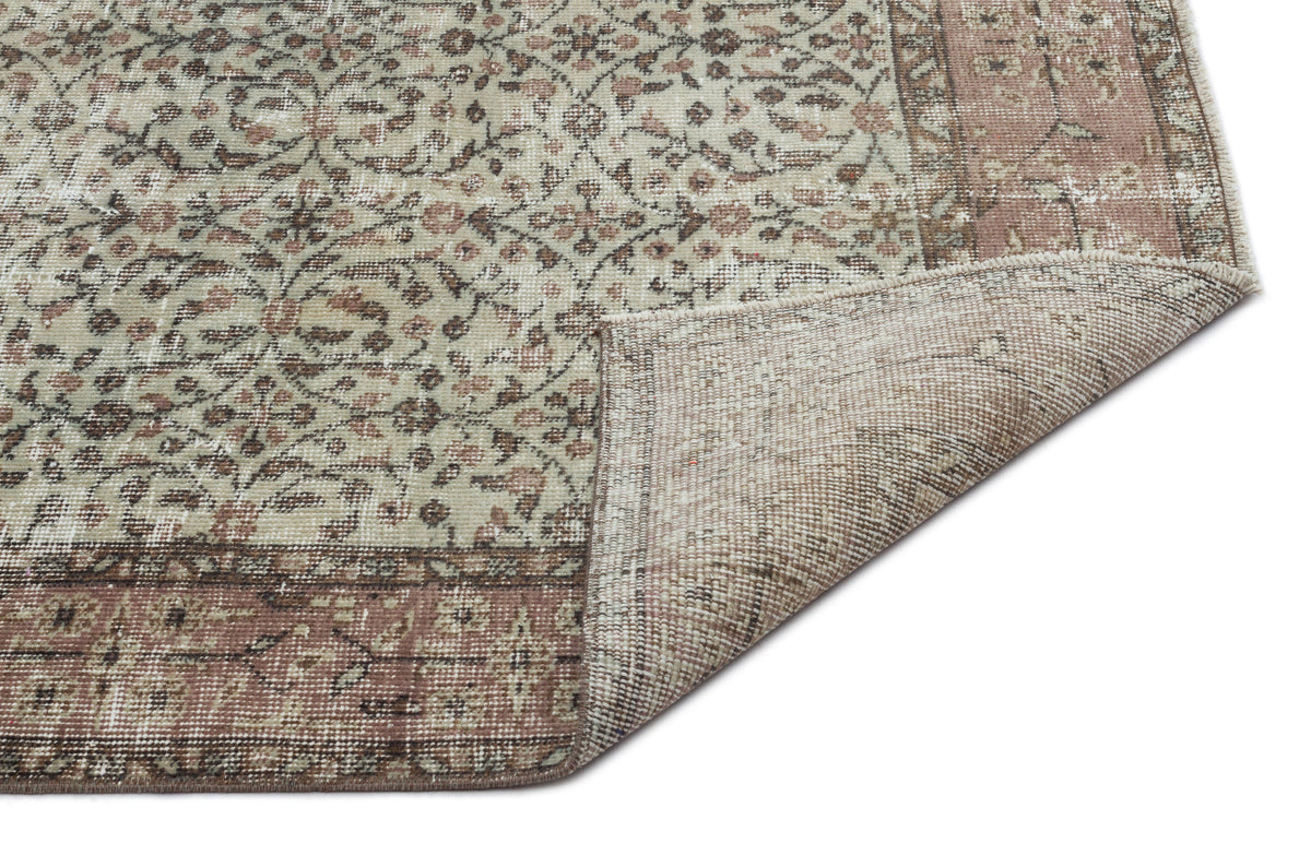 Distressed beige and dusty rose rug with a traditional floral pattern and a folded corner showing the woven backing.