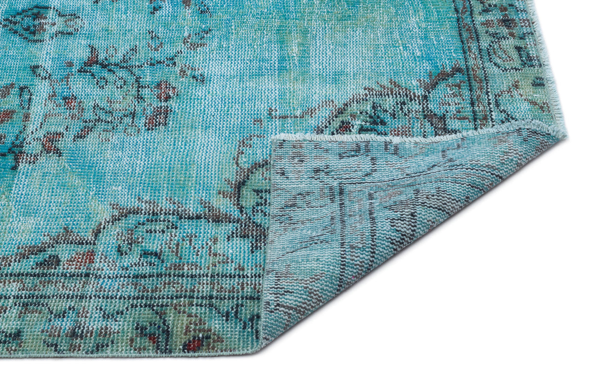 Distressed turquoise rug with a faded floral medallion pattern and a folded corner showing the woven backing.