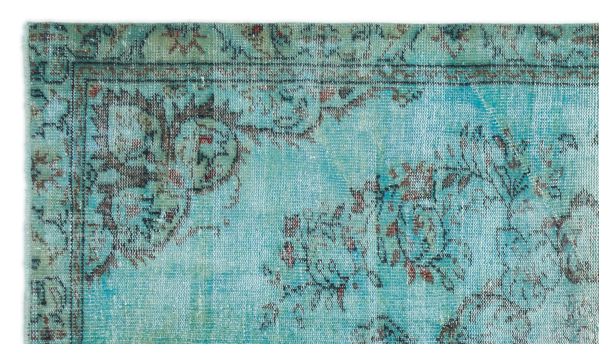 Distressed turquoise rug with a faded floral pattern and dark brown border details.