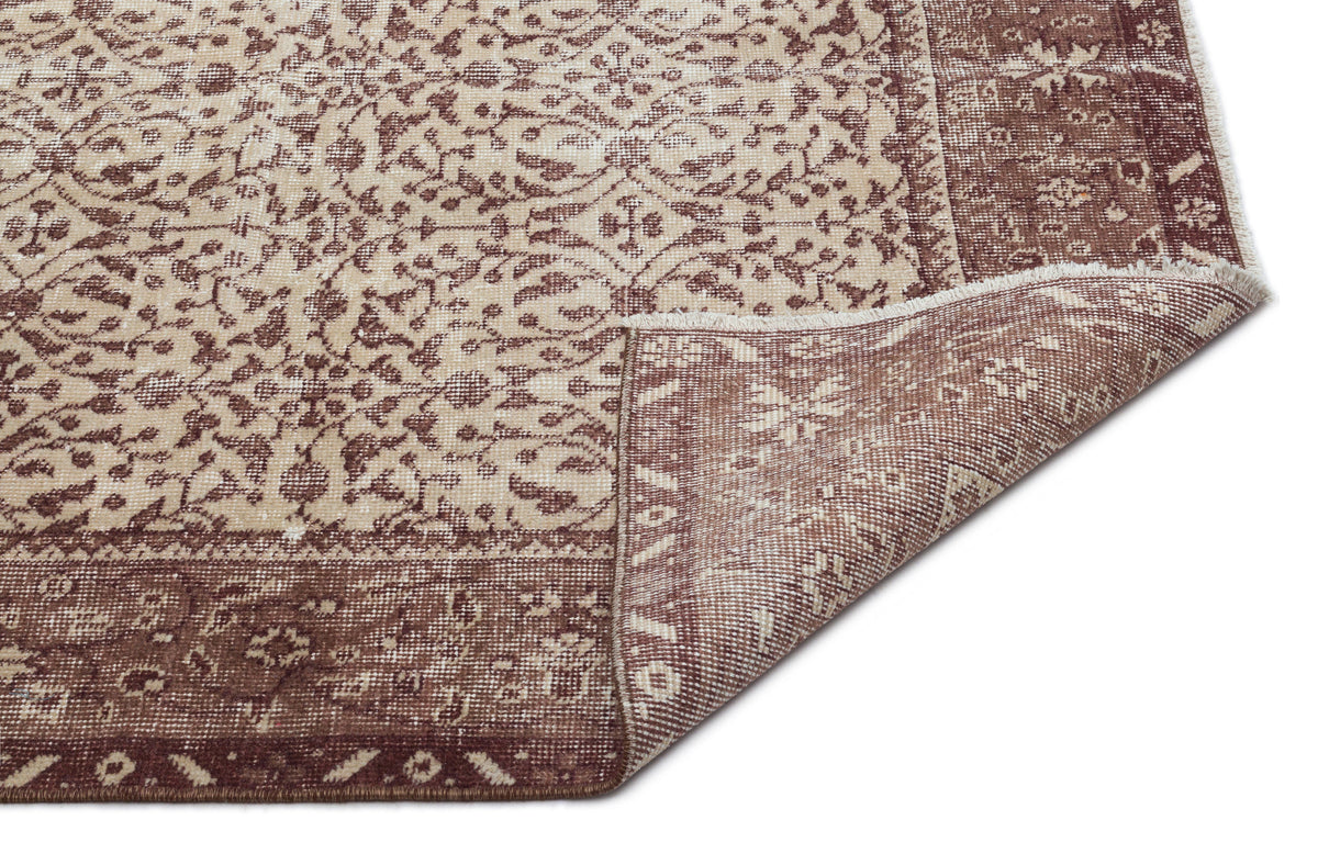 Brown and beige rug with a traditional floral medallion pattern and a folded corner showing the woven backing.