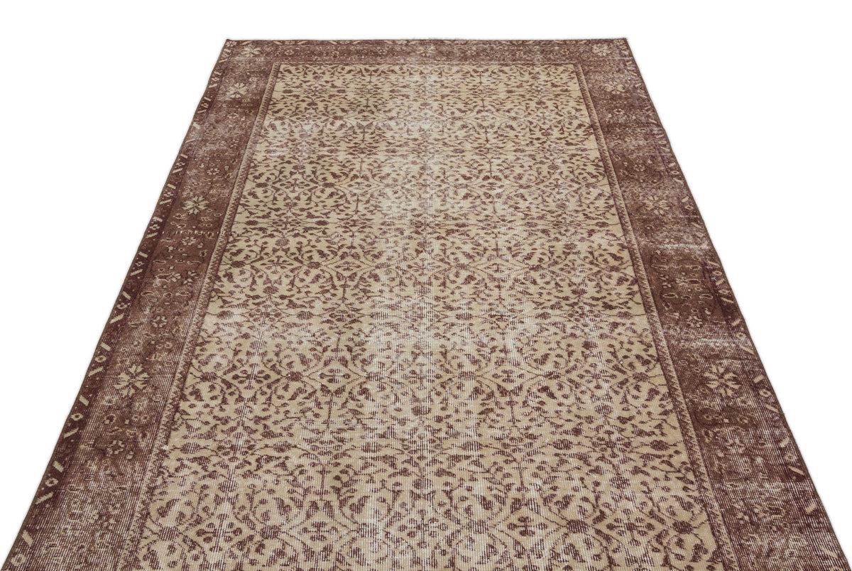 Brown and beige vintage-style rug with a distressed floral medallion pattern and a wide decorative border.