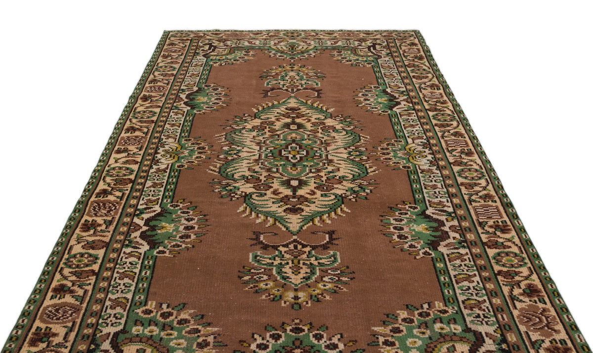 Brown traditional rug with a central green and cream floral medallion and a decorative geometric border.