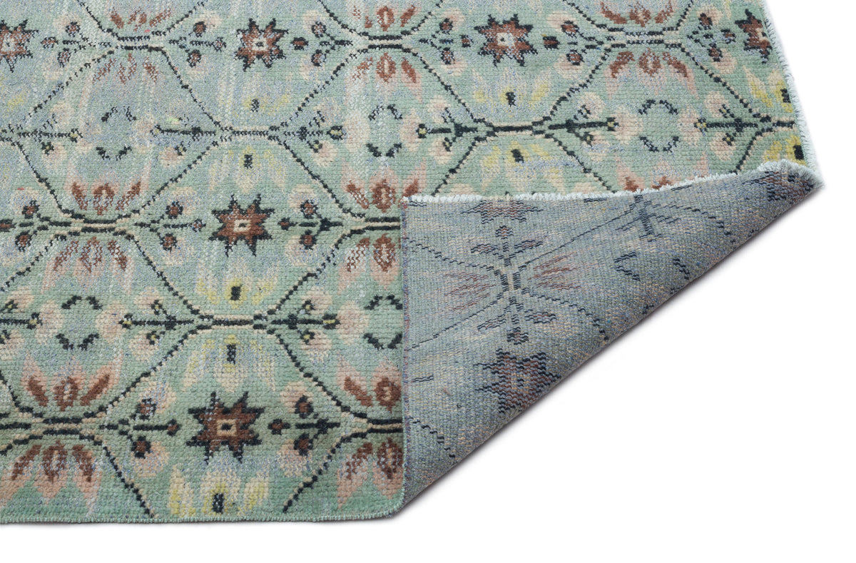 Sage green rug with a distressed floral medallion pattern and a folded corner revealing the textured backing.