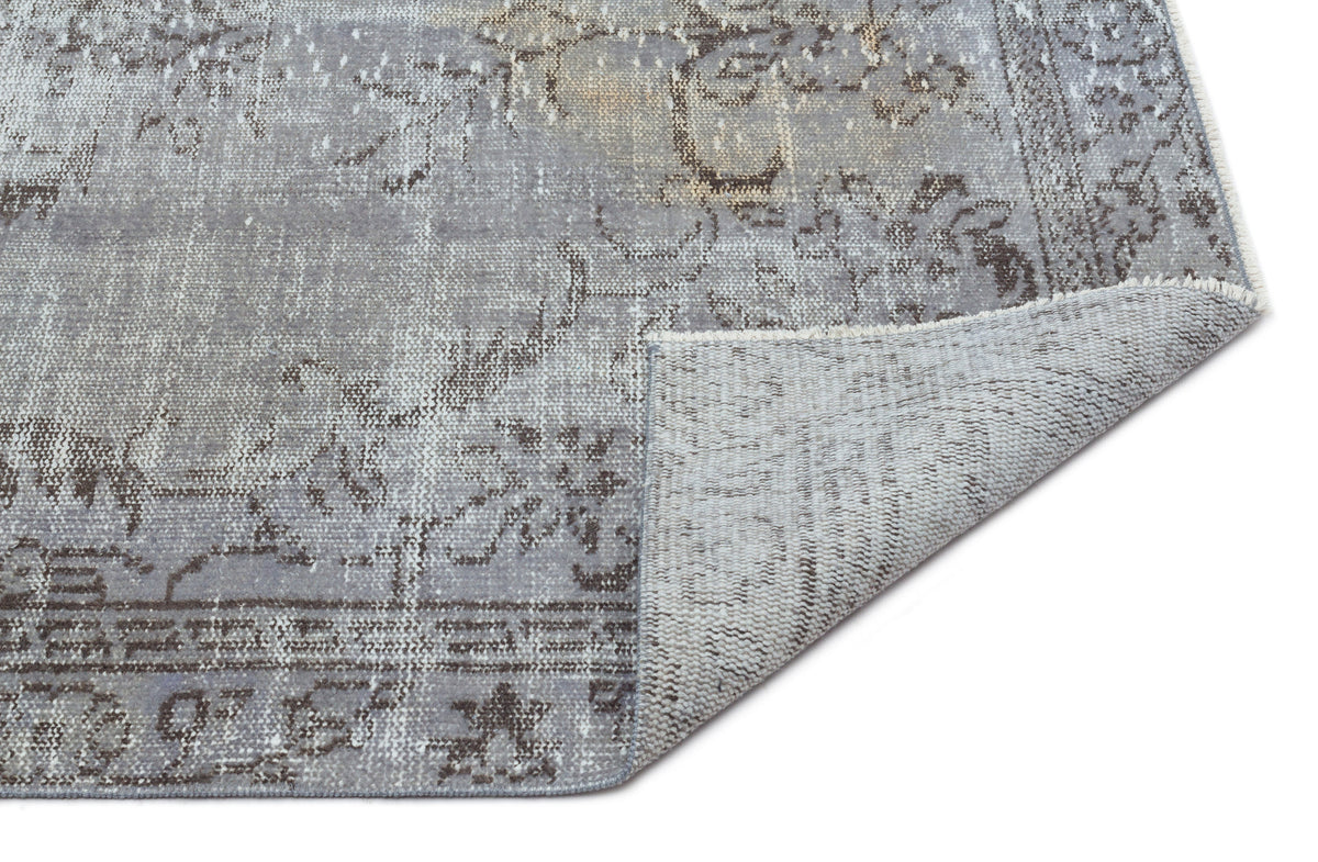 Grey and charcoal distressed traditional rug with a floral medallion pattern, shown with a corner folded over.