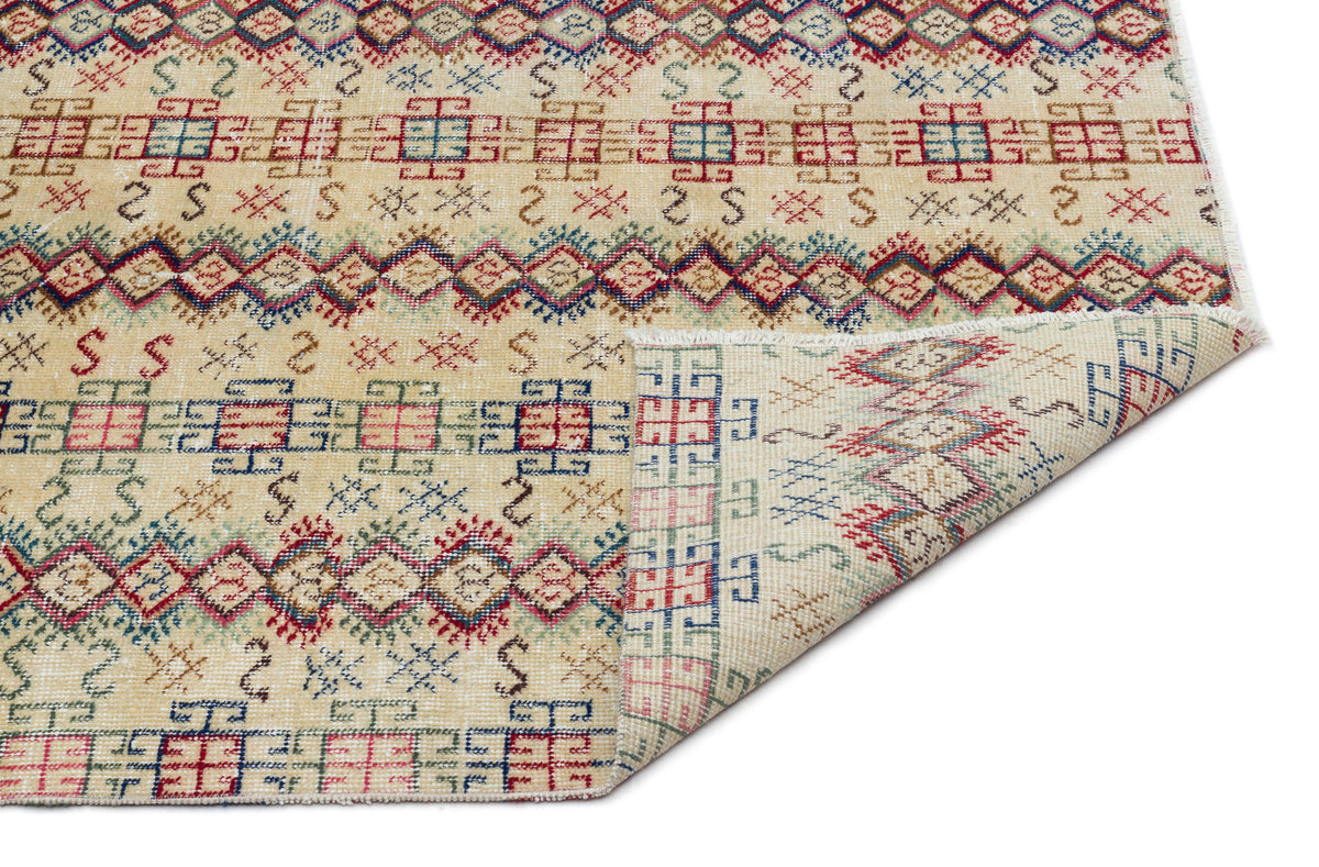 Beige rug with red, blue, and green geometric tribal patterns and a folded corner showing the reverse side.