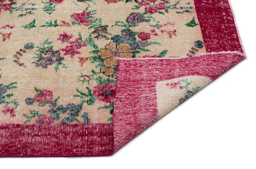 Load image 1 in gallery view. Beige rug with a distressed floral pattern in red, green, and blue, featuring a wide red border and a folded corner.