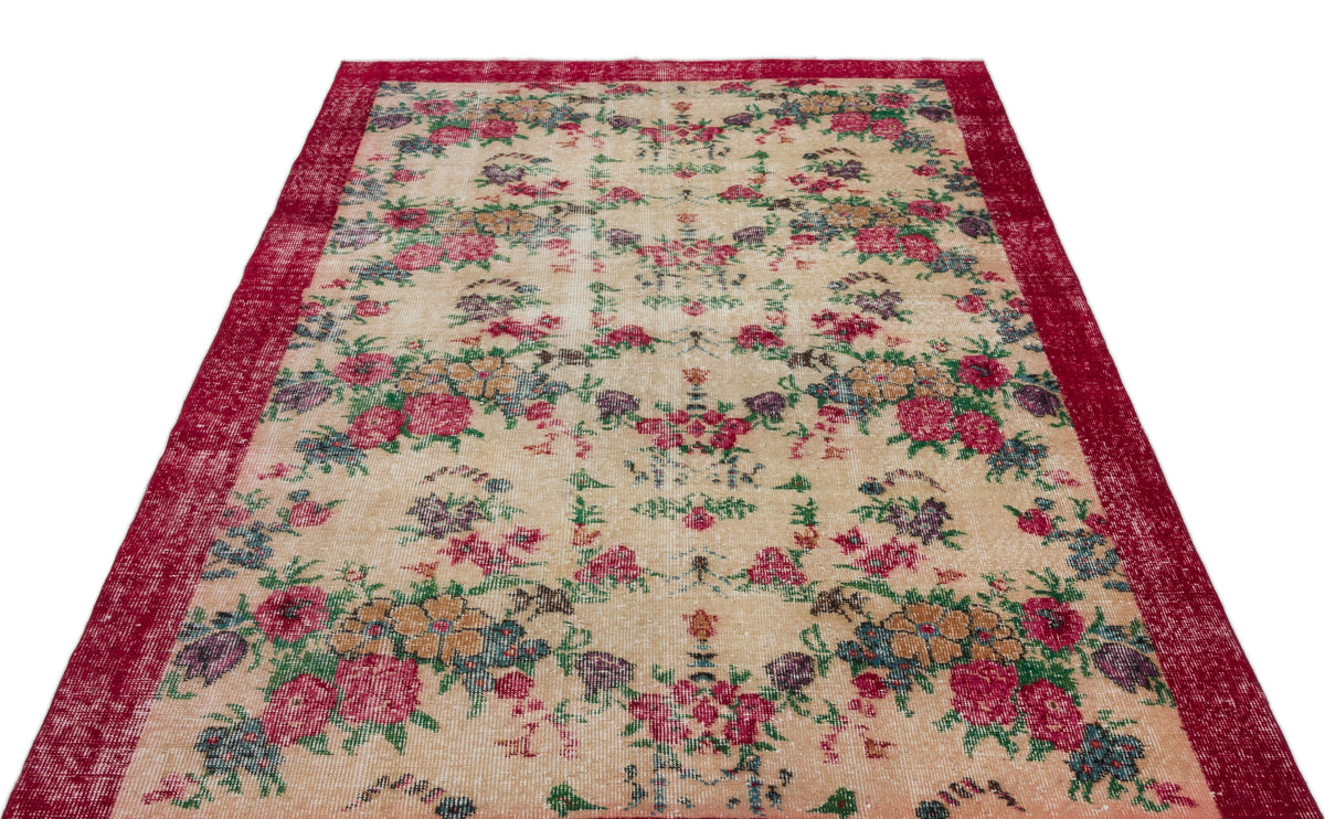 Beige vintage-style rug with a distressed floral pattern in red, green, and purple, featuring a wide red border.