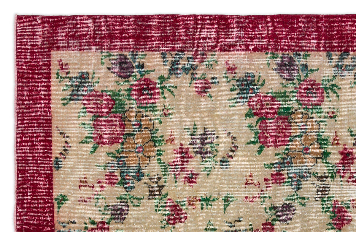 Distressed beige rug with a deep red border and a multi-colored floral pattern in pink, green, and purple.