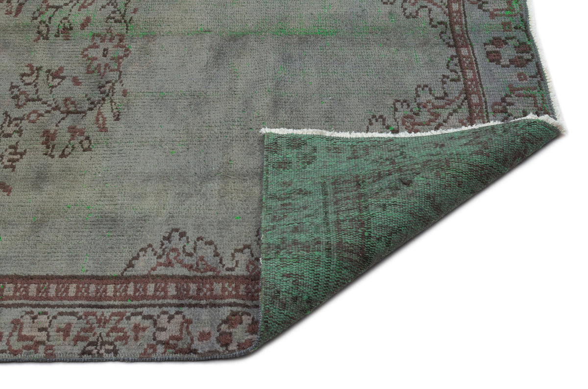 Grey and green distressed rug with a traditional floral border, shown with a corner folded over on a white background.